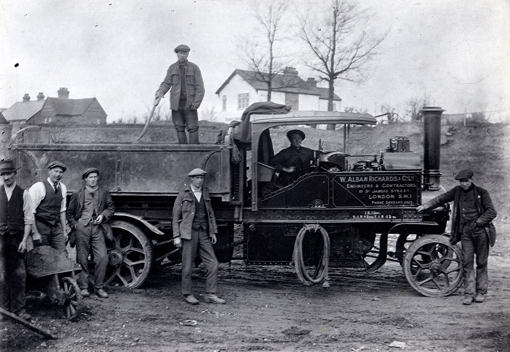 An unidentified Foden wagon seen here in the ownership of W. Alban Richards & Co Ltd, Engineers & Contractors, 19 St James Street, London, SW1. The photo shows the wagon from the offside, four men stand towards the rear, one has a wheelbarrow. There is a man above the others standing in the back of the carrying area on the back of the lorry. Another man stands towards the front of the wagon, leaning against the chassis. The driver is sat looking at the camera. 