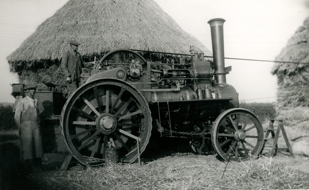 Davey Paxman traction engine No. 15434 in the ownership of Albert Chapman, Ashford. Photo shows the offside, its driver stands on the footplate and a second man stands in front of the tender at the rear. In the background are large hayricks.